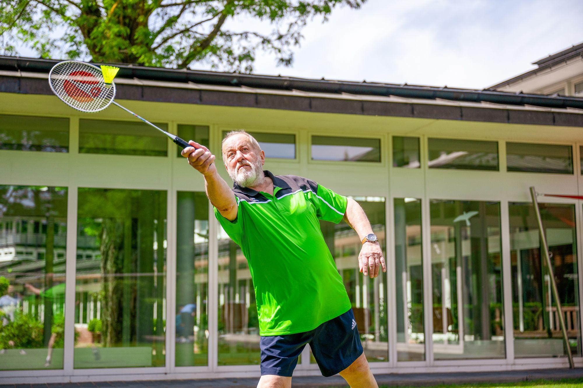 Mann spielt Badminton, im Hintergrund ist die Rehaklinik zu sehen.