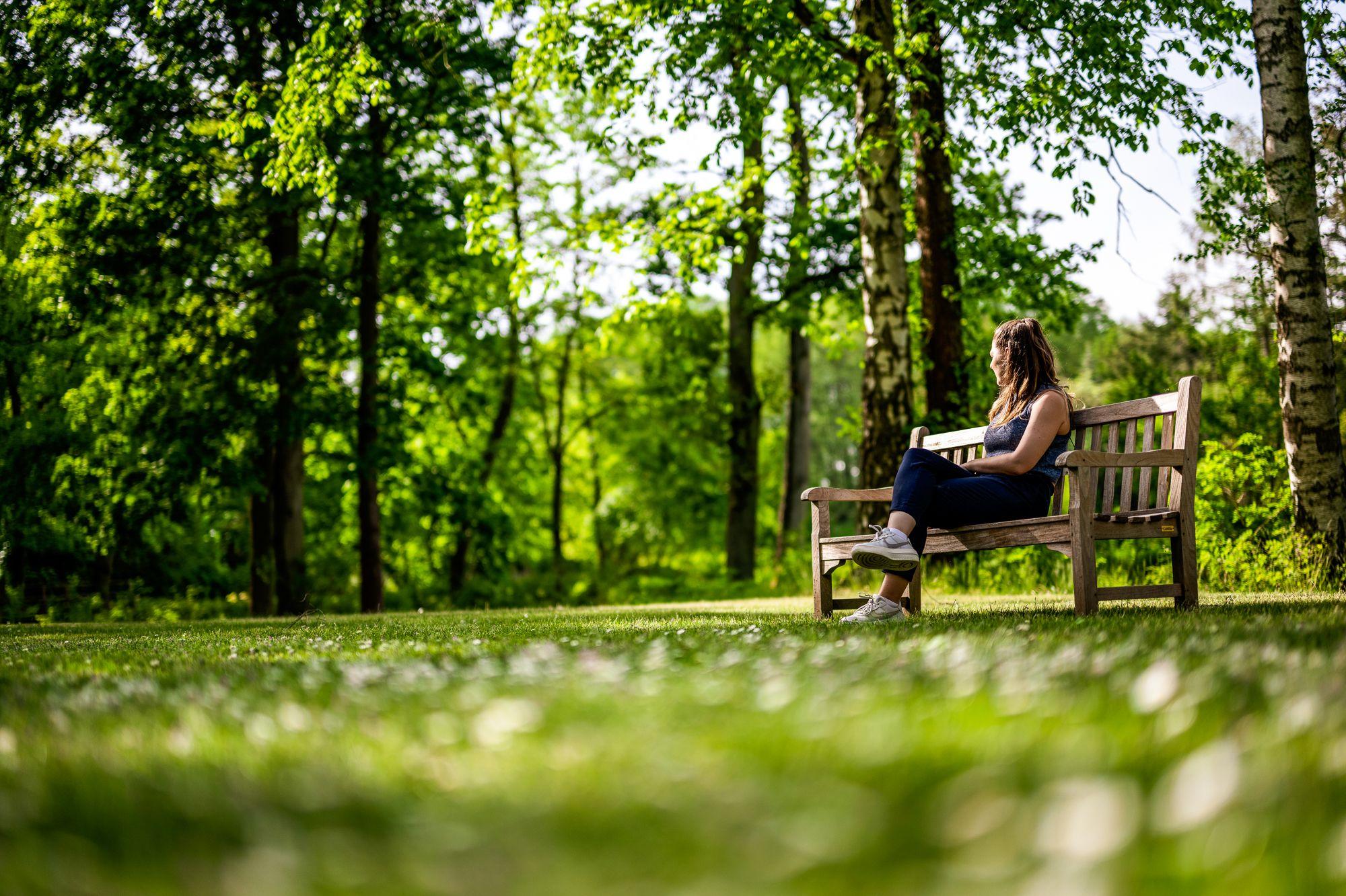 Eine Frau sitzt auf einer Bank im Park der Klinik