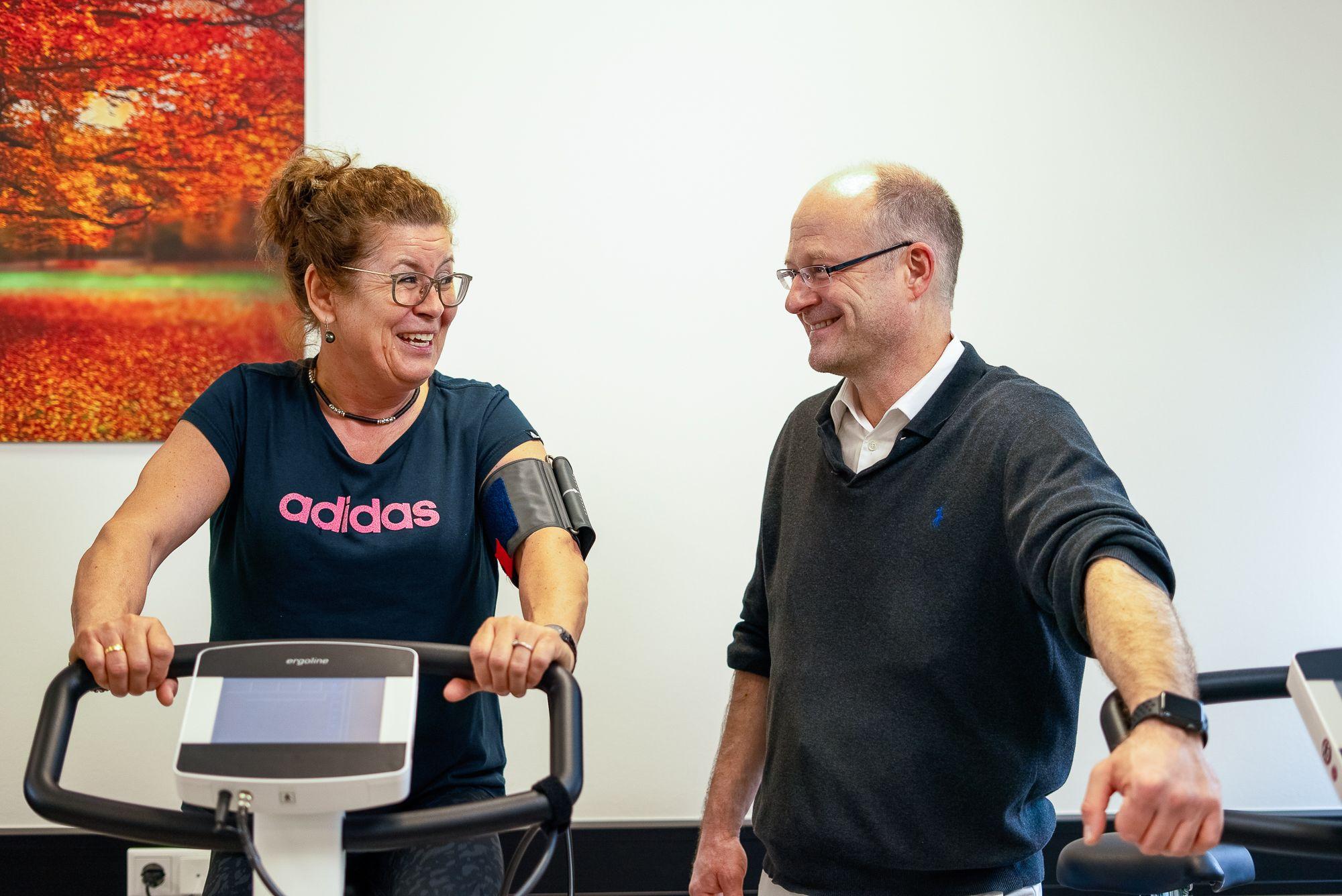 Dr. med. Michael Schäfer berät eine Patientin, die während ihrer Othopädischen Reha auf einem Ergometer trainiert.