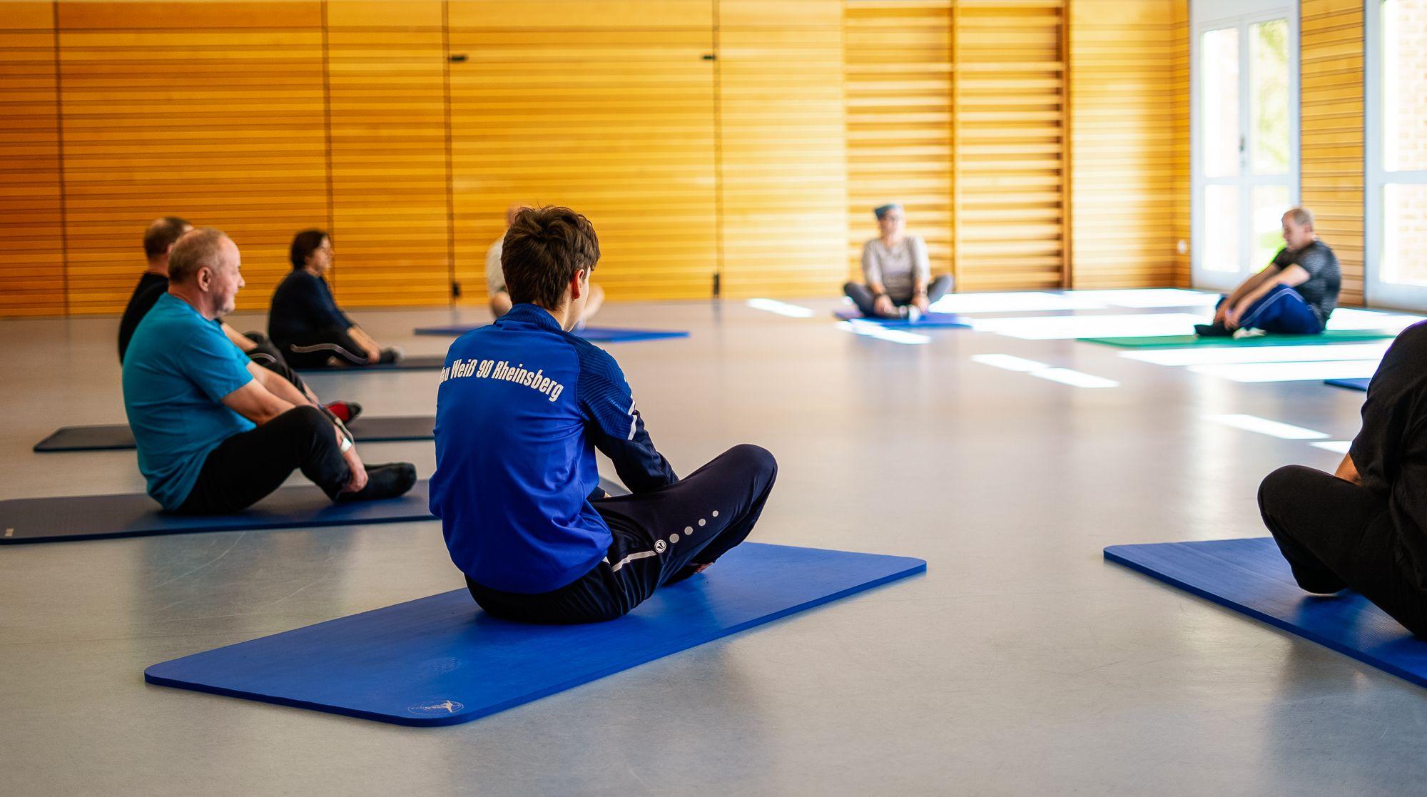 Mehrere Personen sitzen auf Yogamatten im Kreis zusammen 